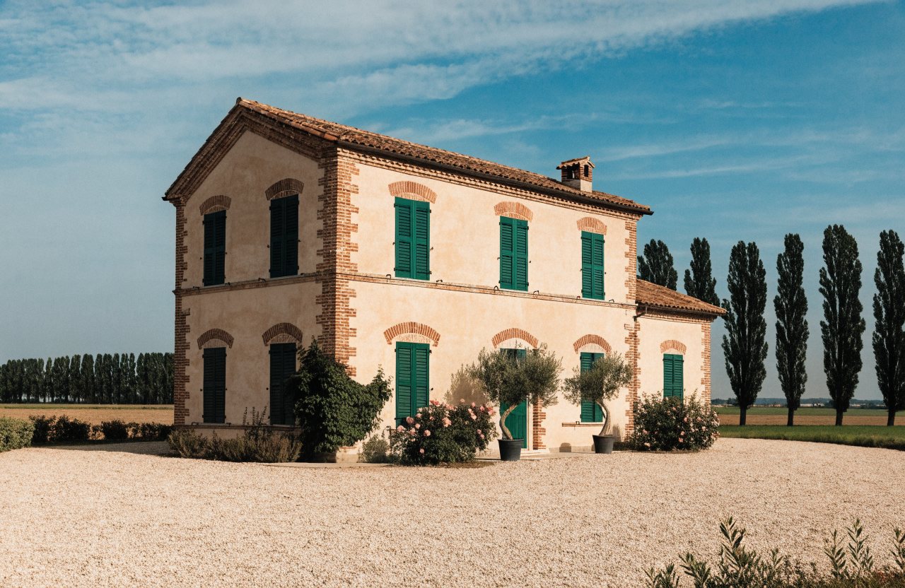 Casa di campagna romagnola restaurata, intonaco chiaro e mattoni a vista, persiane verdi, pioppi e campi sullo sfondo