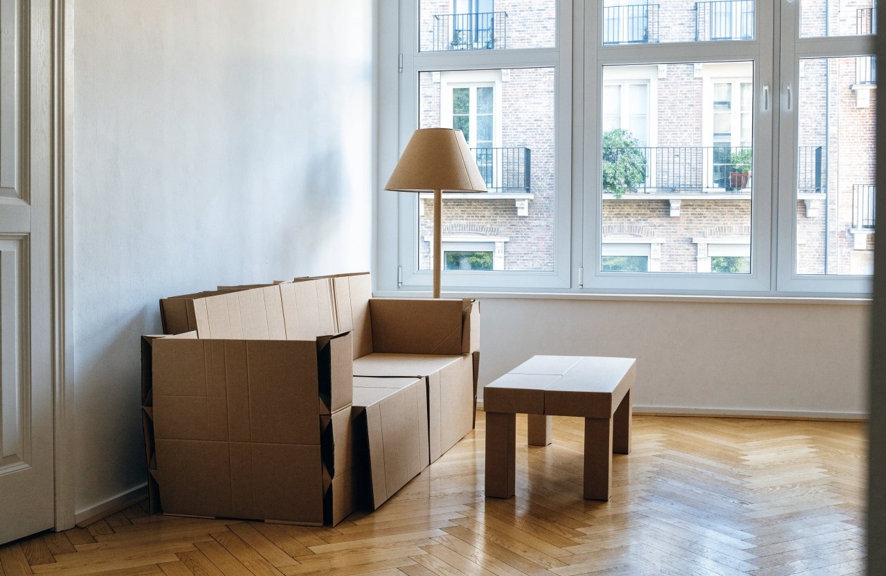Divano, tavolino e lampada di cartone in scala 1:1 davanti a una grande finestra sui palazzi di fronte